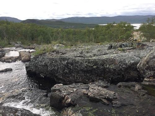 Kivenlohkareita, kalliota ja vettä Tsahkalputouksella. Taustalla Kilpisjärvi.